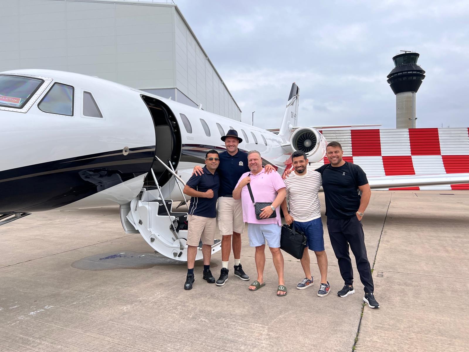 Spencer Brown, Nav Salimian and Tyson Fury with their team beside a private jet while travelling to a boxing event